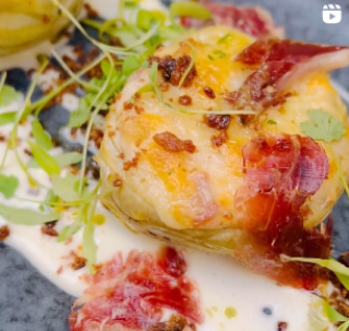 Close-up of a dish with prosciutto-wrapped food, garnished with herbs and creamy sauce.